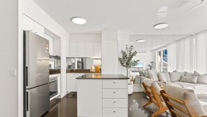 A modern kitchen with white cabinetry, a stainless steel refrigerator, and a central island with a sink. - Penthouse 20 - The Cove (Noosa)