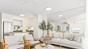 A modern living room with a sofa, two armchairs, a coffee table, and a kitchen area in the background. - Penthouse 20 - The Cove (Noosa)
