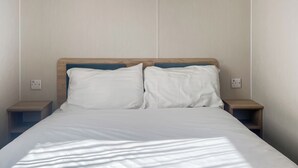 A bed with white linens and two pillows, flanked by wooden nightstands with a power outlet on each.