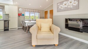 Un salon avec un canapé beige, un coin repas avec une table et des chaises, une cuisine avec un réfrigérateur et une grande fenêtre.