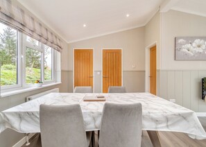 A dining room with a marble table, grey chairs, wooden doors, and a window with a view of greenery.