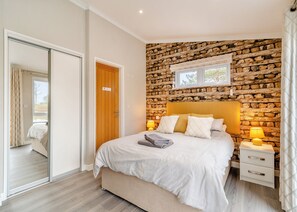 A bedroom with a stone wall, a bed, a nightstand, a window, and a door.