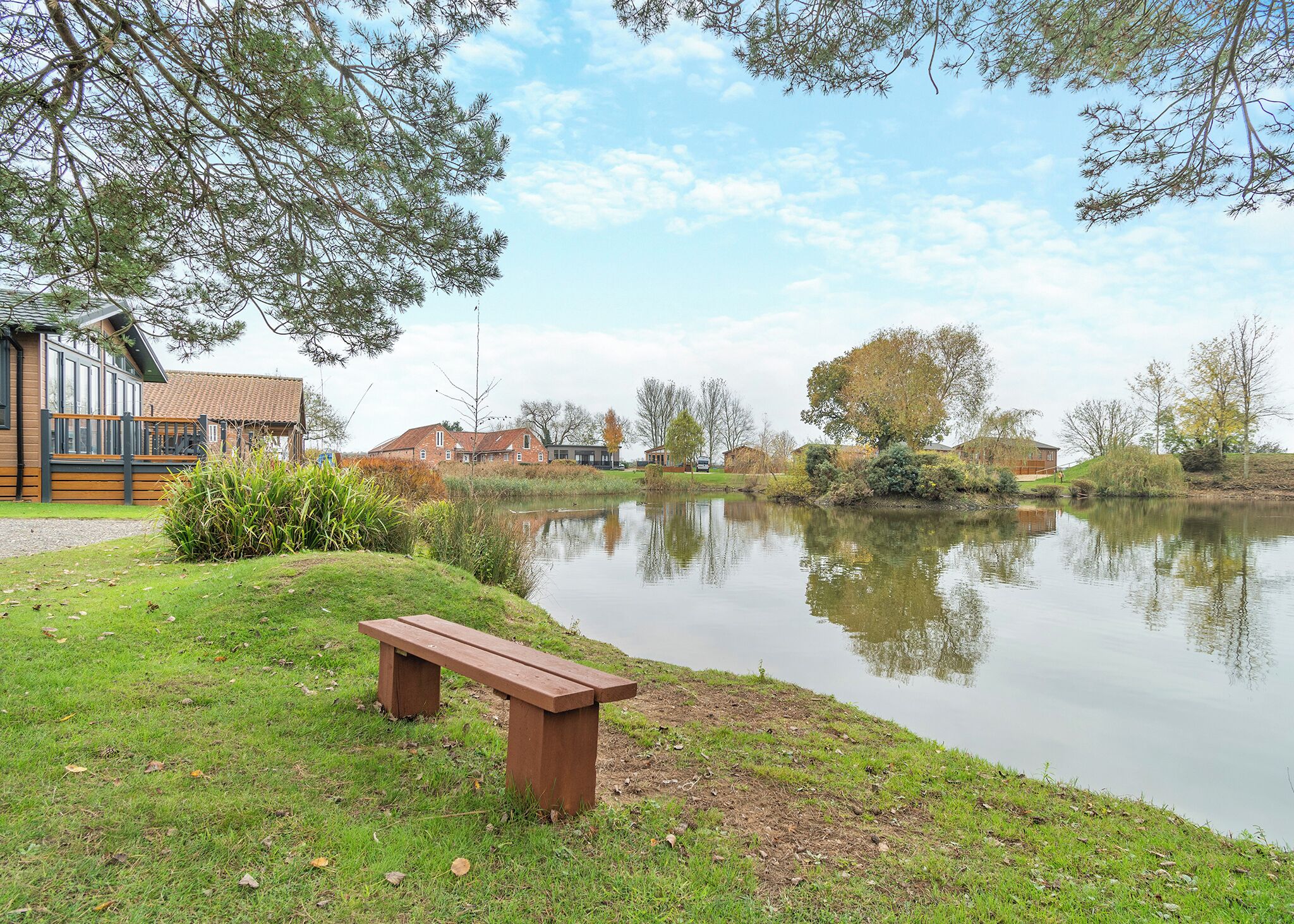 A lakeside view with a wooden bench, a building with a tiled roof, and a clear sky.