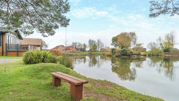 A lakeside view with a wooden bench, a building with a tiled roof, and a clear sky.