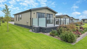 A row of modern, single-story mobile homes with large windows, a grassy lawn, and a clear sky. - 2 bedroom accommodation in Midsomer House, East Compton (Midsomer House, East Compton)