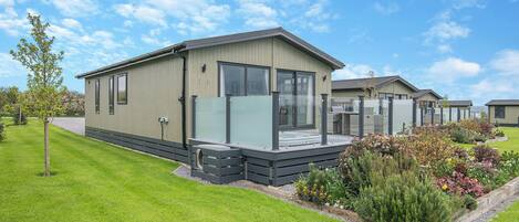 A row of modern, single-story mobile homes with large windows, a grassy lawn, and a clear sky.