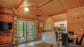 Interior d'una cabana de fusta amb saló, zona de menjador, cuina i portes corredisses de vidre que donen a una terrassa.