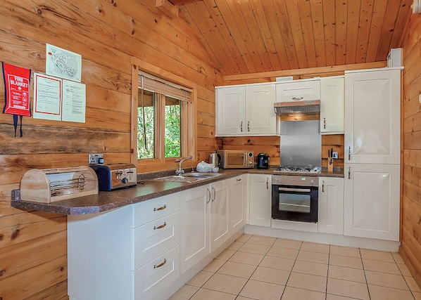 A wooden cabin kitchen with a sink, stove, microwave, and cabinets.