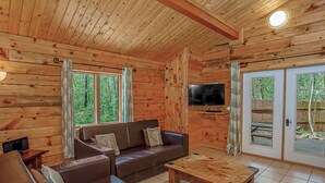 Interior d'una cabana de fusta amb un sofà, una televisió i una taula de dinar.