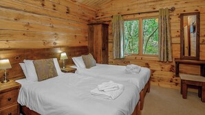 Un dormitori de cabana de fusta amb dos llits, una tauleta de nit amb una làmpada, un mirall i una finestra amb cortines.