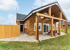 Eine Blockhütte mit einer Steinterrasse, einem Holzdeck und einer überdachten Sitzgruppe im Freien.