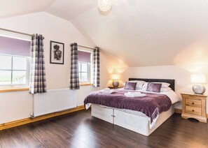 Ein Schlafzimmer mit einem großen Bett, zwei Nachttischen, einem fenster mit Vorhängen, einem Heizkörper und einer Deckenleuchte.