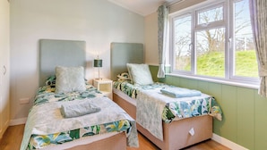 Un dormitorio con dos camas, una ventana con cortinas, una lámpara de noche y una lámpara colgante.