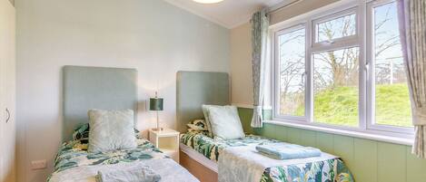 A bedroom with two beds, a window with curtains, a bedside lamp, and a hanging light fixture.