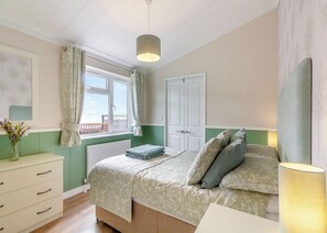 Un dormitorio con cama, cómoda, ventana con cortinas y vista al exterior.