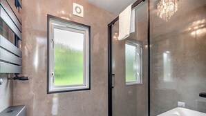 Une salle de bain moderne équipée d’une douche, de toilettes, d’un lavabo et d’une fenêtre donnant sur un espace verdoyant.