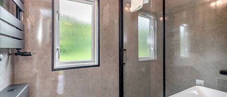 Ein modernes Badezimmer mit Dusche, Toilette, Waschbecken und einem Fenster mit Blick auf Grünflächen.
