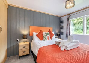 A bedroom with a bed, bedside tables, a headboard, a window, and a view of greenery outside.