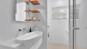 Ein modernes Badezimmer mit einem weißen Waschbecken, einem Spiegel und Holzregalen darüber.