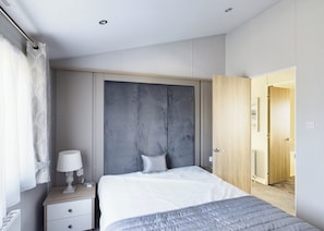 A modern bedroom with a large bed, a bedside table with a lamp, and a wardrobe with a grey panel design. - Platinum Lodge 4 Hot Tub (Skegness)