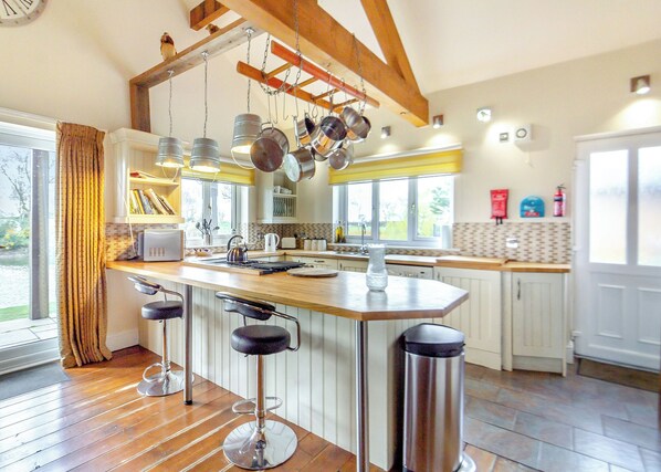 A kitchen with a central island, bar stools, hanging pots, and a window with curtains. - Traditional two bedroomed lodge with two double rooms. (Swinethorpe, Nr Lincoln)