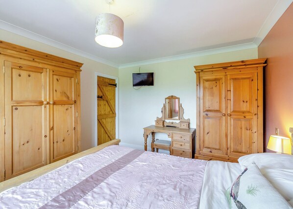 Ein Schlafzimmer mit Bett, Holzschrank, Schminktisch, Fernseher und Lampe.
