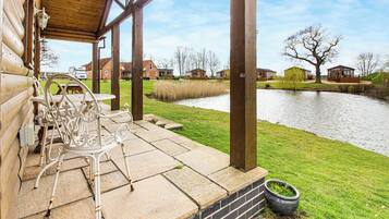 A wooden deck with outdoor seating, a brick wall, and a view of a river and houses in the background.