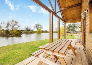 A wooden deck with picnic tables overlooking a calm lake, surrounded by trees and a grassy area. - Traditional two bedroomed lodge with two double rooms. (Swinethorpe, Nr Lincoln)