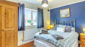 A bedroom with a bed, a window with curtains, a radiator, a wooden wardrobe, and a painting on the wall.