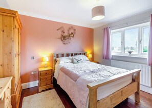 A bedroom with a wooden bed, bedside lamps, a wall-mounted light fixture, a window with curtains, and a radiator. - Traditional two bedroomed lodge with two double rooms. (Swinethorpe, Nr Lincoln)