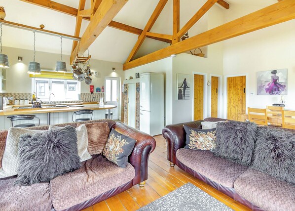 A spacious living area with a high ceiling and exposed beams, a kitchen in the background, and a dining area with wooden furniture. - Traditional two bedroomed lodge with two double rooms. (Swinethorpe, Nr Lincoln)