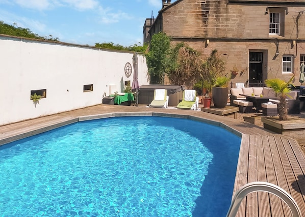 A swimming pool with a wooden deck, lounge chairs, and a stone building in the background.