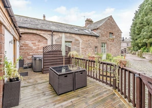 A stone building with a wooden deck, outdoor seating, and a view of a cobblestone street.