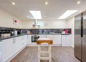 A modern kitchen with white cabinets, a wooden table, a stainless steel refrigerator, and a skylight.