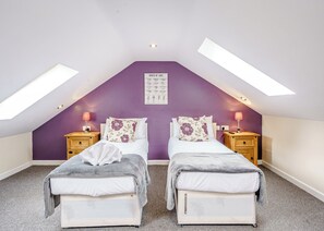 Une chambre avec deux lits, un mur d’accent de couleur violette et des fenêtres de toit.