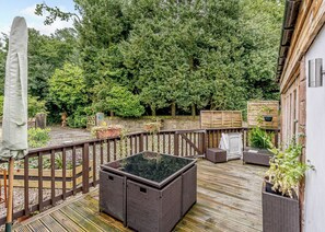 Eine Holzterrasse mit Korbmöbeln, einem Glastisch und Topfpflanzen.
