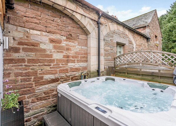 Une construction en pierre avec une clôture en bois, un jacuzzi et une terrasse en bois.