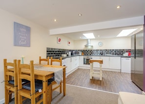 A modern kitchen with white cabinets, a wooden dining table, and a built-in microwave.
