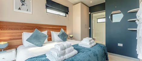 A modern bedroom with a wooden headboard, a large bed with blue bedding, a bedside table with a lamp, and a shower area.