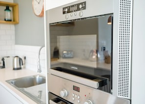 A kitchen with a built-in oven, a stainless steel kettle, and a sink.