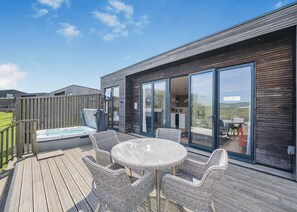 A modern outdoor deck with a hot tub, wicker furniture, and a view of the interior.