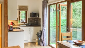 Une cuisine moderne équipée d’un four à micro-ondes, d’un évier et de placards, un coin repas avec une table et des chaises, et une porte-fenêtre coulissante donnant sur un balcon agrémenté de verdure.