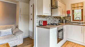 Une cuisine de taille modeste, avec des meubles blancs, un grille-pain rouge, une cuisinière à gaz et une fenêtre donnant sur un beau paysage.