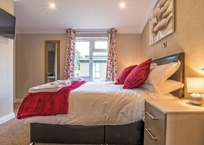 A bedroom with a bed, a nightstand, a lamp, and a window with curtains.