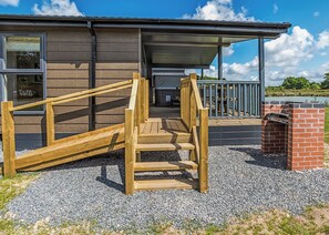 A wooden staircase leading to a covered area with a brick structure, gravel ground, and a building with windows and a metal roof.