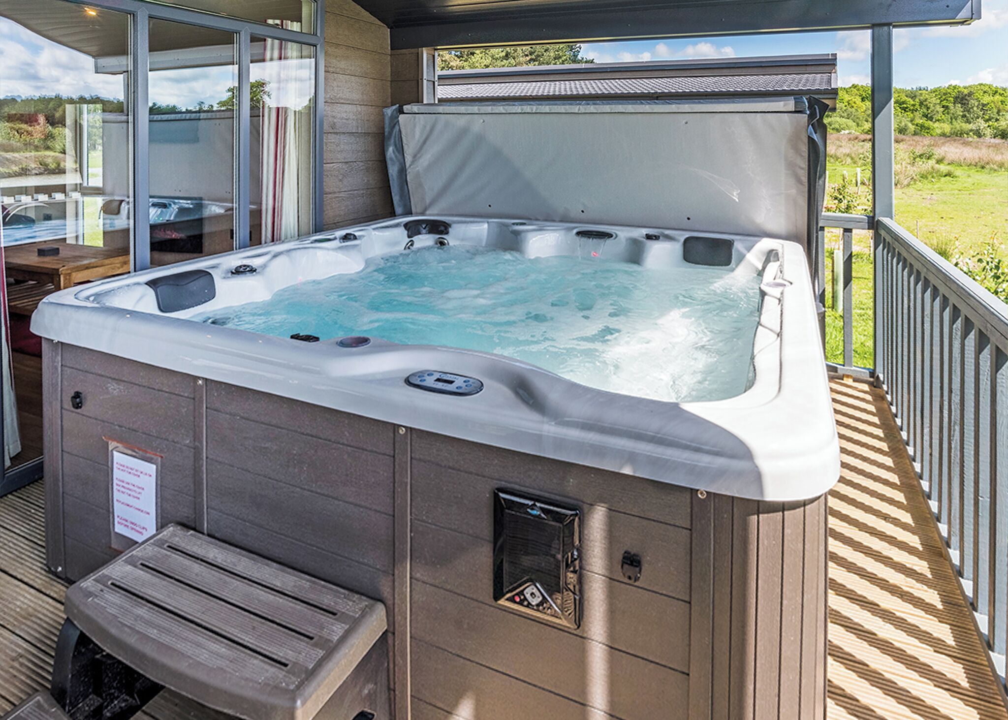 Een hottub op een terras met een houten bank, glazen deuren en uitzicht op het omliggende landschap.