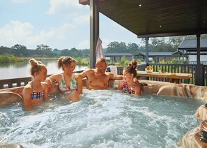 Ein Whirlpool mit vier Personen, umgeben von einer Holzterrasse und Blick auf einen See.