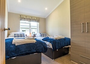 A bedroom with two beds, a window with blinds, a wardrobe, and a door.