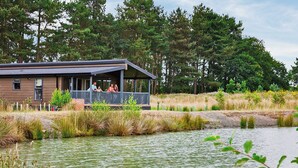 Un chalet au bord du lac, doté d’une véranda et entouré de grands arbres, avec un plan d’eau paisible à proximité.