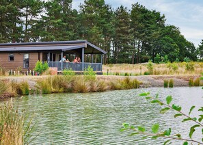 A lakeside cabin with a porch, surrounded by tall trees and a calm water body.